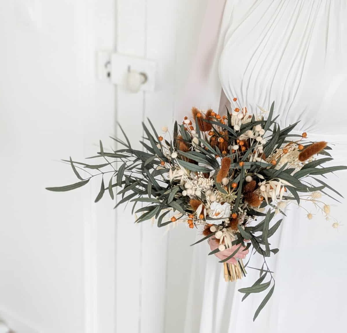 Bouquet de mariée en fleurs séchées et stabilisées aux teintes terra cotta, vert eucalyptus et beiges.