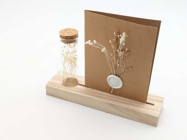 Porte carte en bois avec une éprouvette en fleurs séchées blanches , carte en kraft brun avec fleurs séchées blanches et cachet de cire.