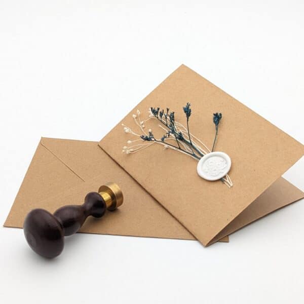Carte en kraft brun avec fleurs séchées bleues et cachet de cire avec enveloppe.