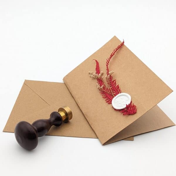 Carte en kraft brun avec fleurs séchées rouges et cachet de cire et enveloppe en kraft brun.