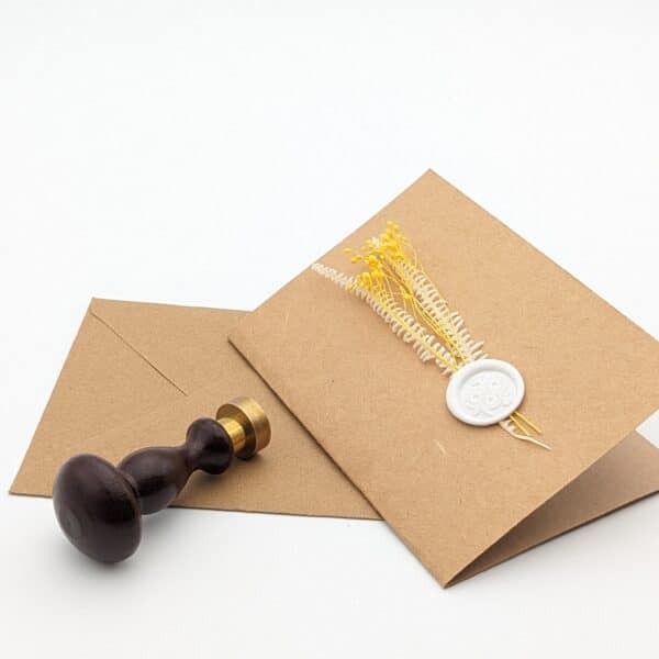 Carte en kraft brun avec fleurs séchées jaunes et cachet de cire avec enveloppe.