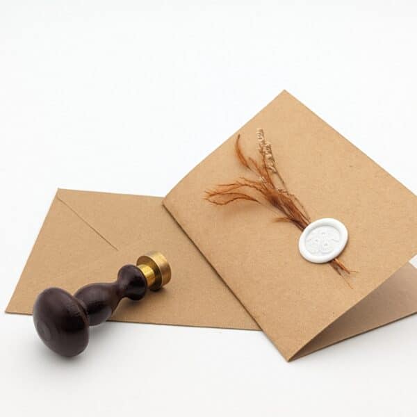 Carte en kraft brun avec fleurs séchées terracotta et cachet de cire avec enveloppe.
