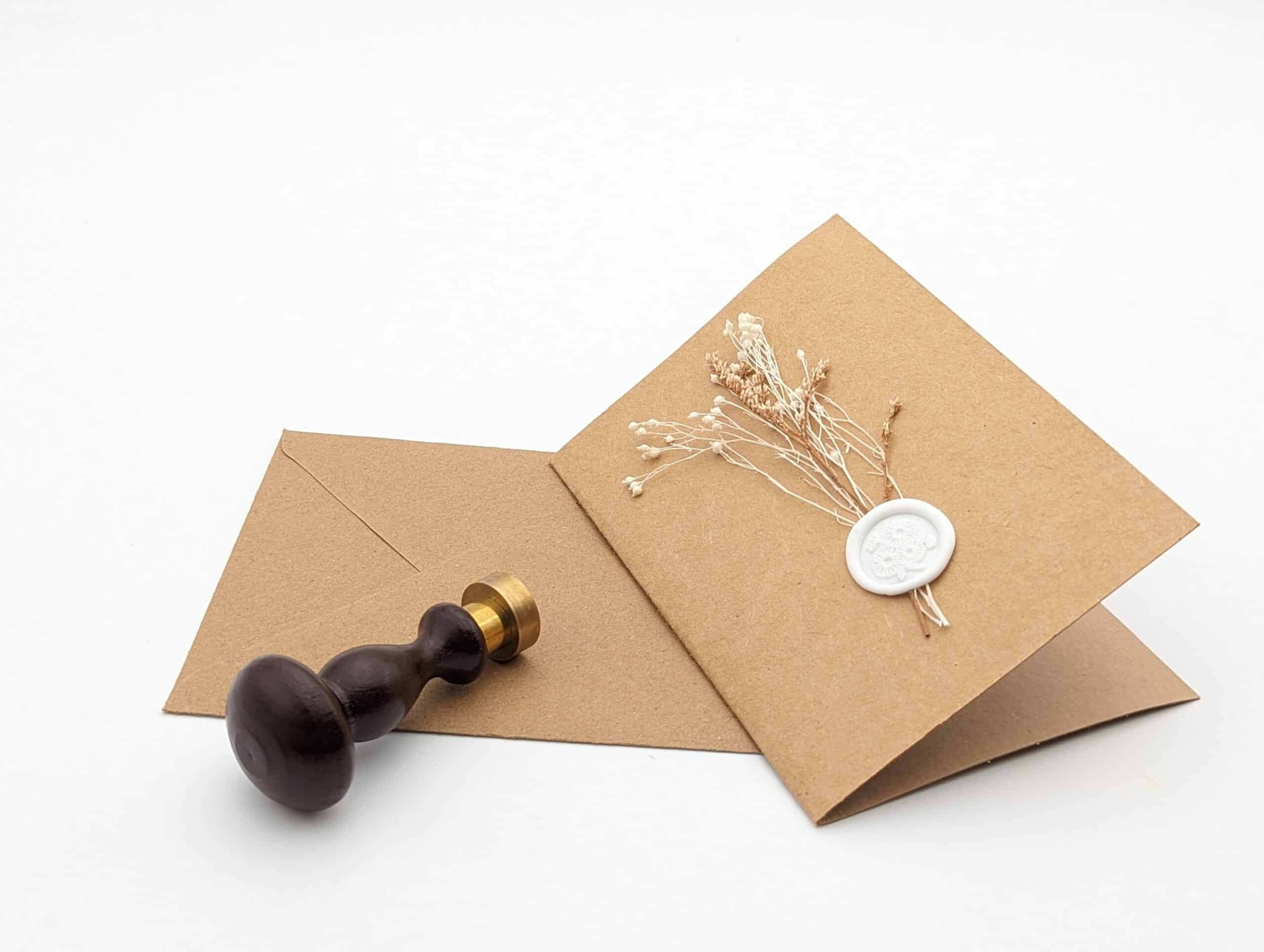 Carte en kraft brun avec fleurs séchées blanches et cachet de cire avec enveloppe.