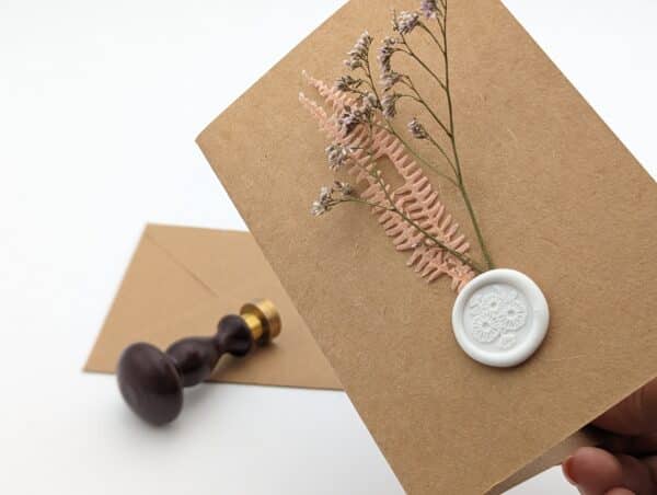 Carte en kraft brun avec fleurs séchées roses et cachet de cire avec enveloppe.