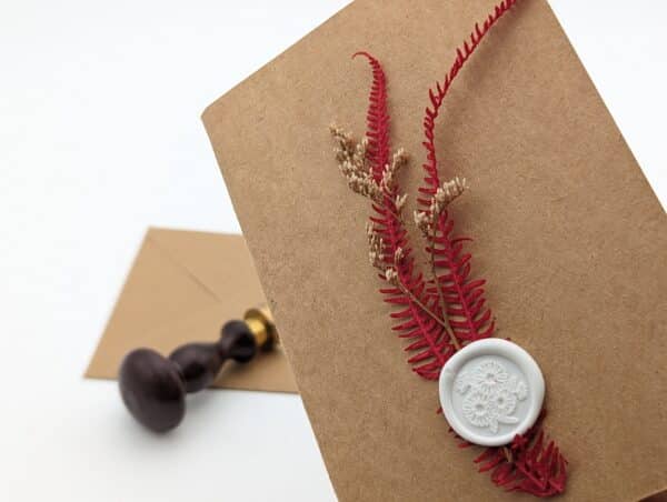 Carte en kraft brun avec fleurs séchées rouges et cachet de cire avec enveloppe.