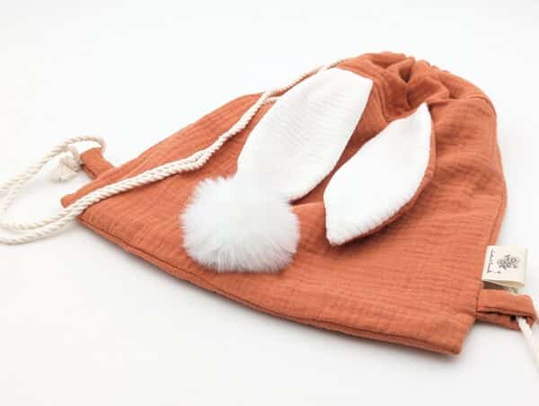 Petit sac pour enfant en double gaze de coton terracotta avec oreille de lapin et queue de lapin en fourrure blanche.