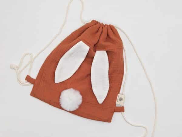 Petit sac pour enfant en double gaze de coton terracotta avec oreille de lapin et queue de lapin en fourrure blanche.