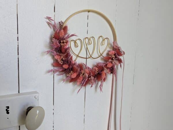 couronne de fleurs séchées aux teintes rose et lilas intérieur avec trois cœurs dorés, cercle en bois